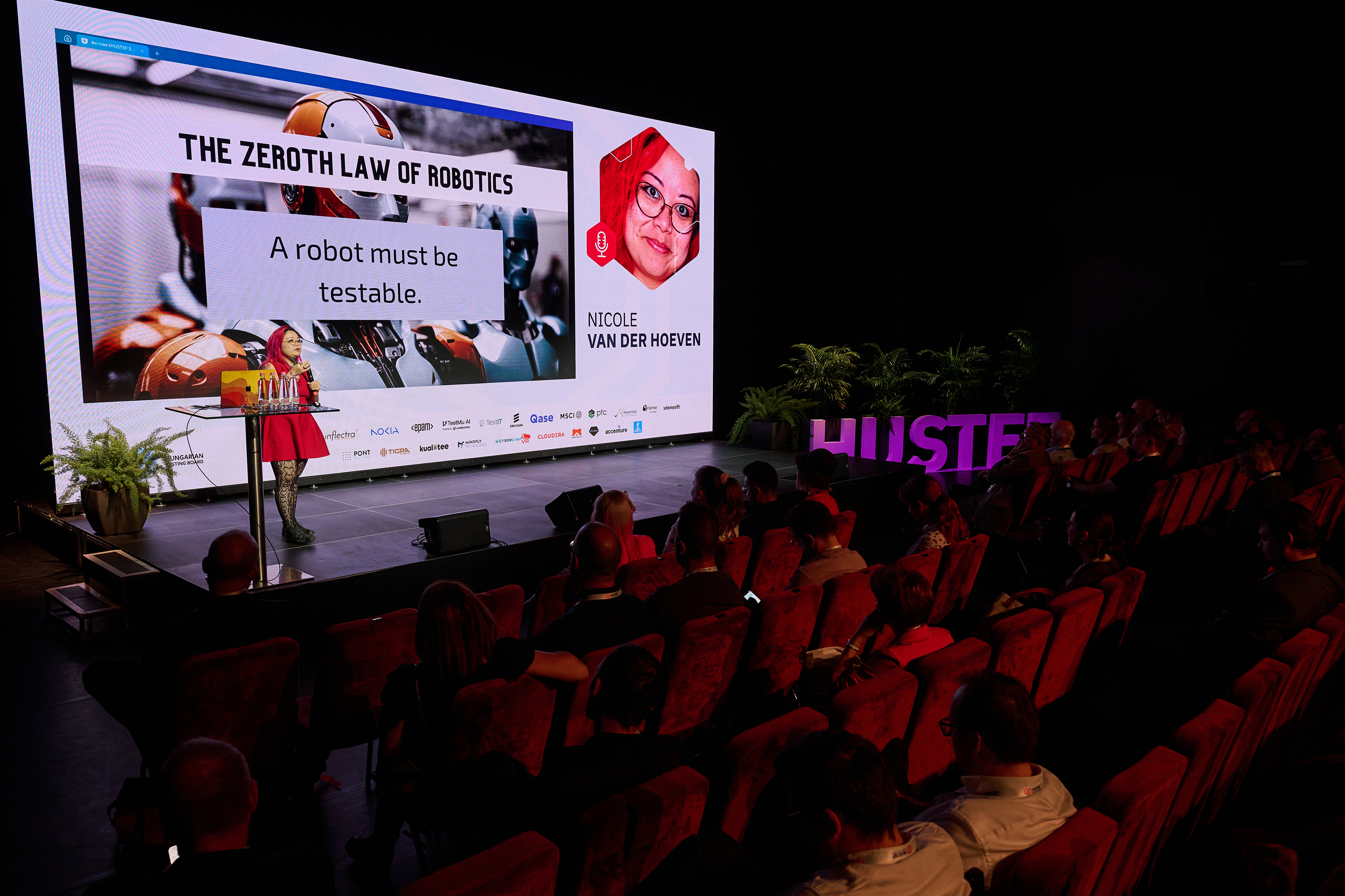Wide shot of me presenting the keynote at HUSTEF 2026, with the title slide reading “The Zeroth Law of Robotics: A robot must be testable” on the big screen above a full audience.